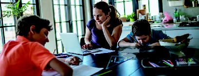 vrouw met immuun trombocytopenie zit aan tafel met haar 2 kinderen. De kinderen maken hun huiswerk en zij werkt op haar laptop